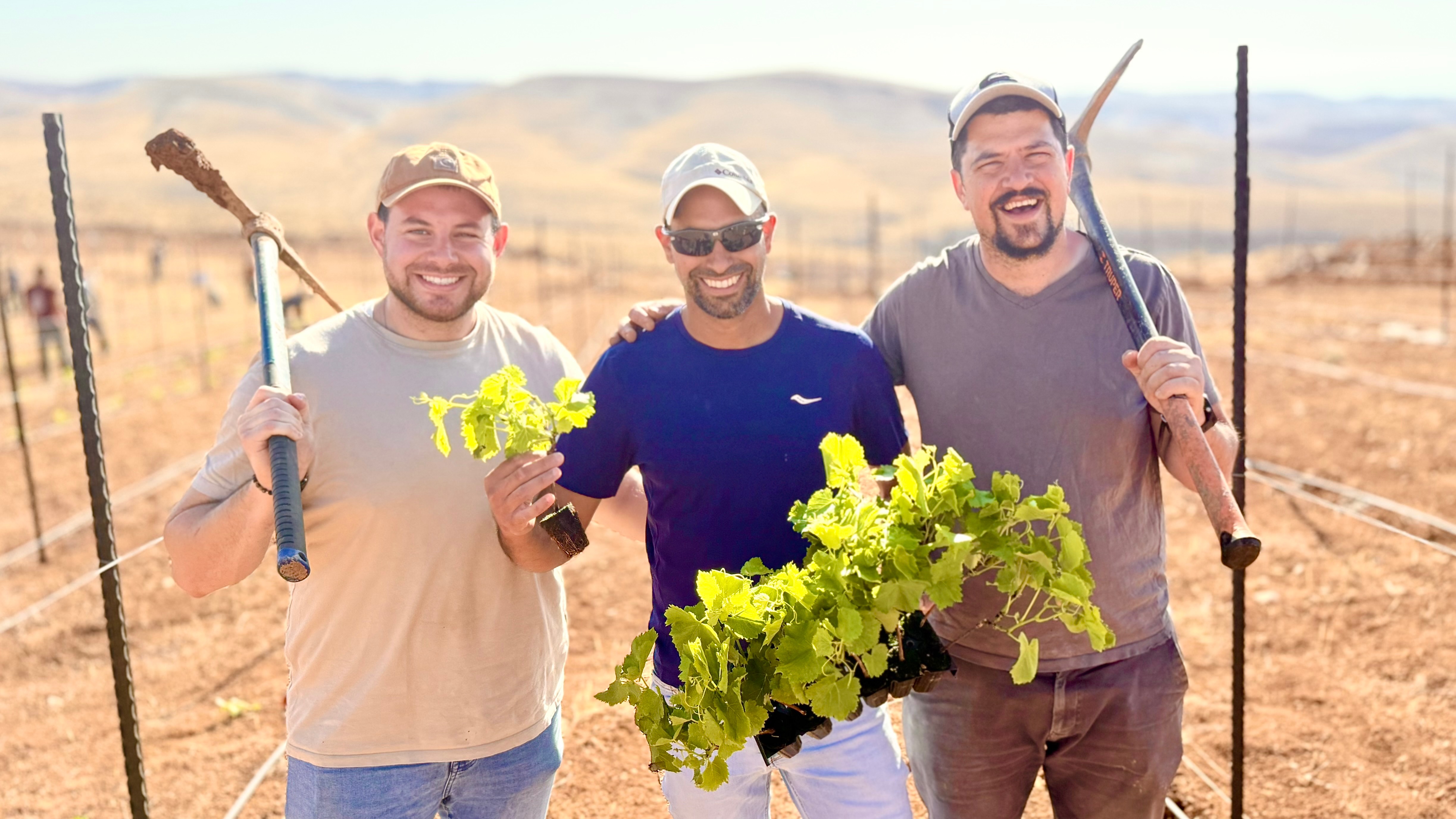 Smiling friends holding vines and tools at the vineyard